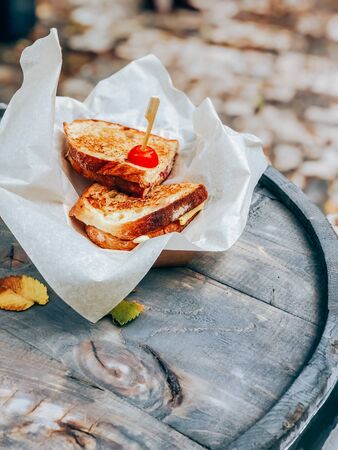 Toasted panini with ham and cheese served on sandwich paper on a wooden outdoor table. Street market food take away conceptの写真素材
