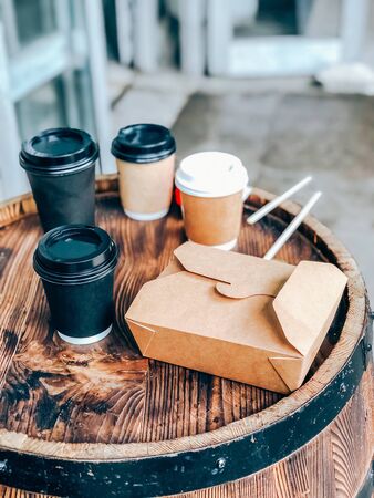Coffee cups and street food craft paper container on a wooden outdoor table. Street market food and drinks take away waste problem concept. Mobile photographyの写真素材