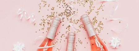 Christmas or New Year composition with bottles of rose champagne and golden shiny sparkle star confetti on pastel pink background, top view. Celebration flat lay. Party creative conceptの写真素材