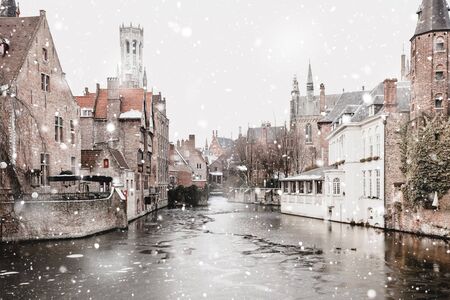 Bruges, Belgium canals view in winter snowfall. Stunning fairy landscape with historical buildings and calm icy water. Christmas mood. Monochromatic neutral tones with natural lightの写真素材