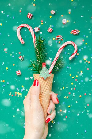 New Year Christmas Xmas holiday celebration woman hand red manicure holding waffle cone candy canes fir tree branch copy space green color paper background. Template greeting card 2020の写真素材