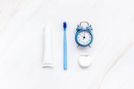 Teeth hygiene and oral dental care products with blue alarm clock on white marble table background with copy space. Blank tube of toothpaste and brushes. Flat lay, top view knolling composition mockupの写真素材