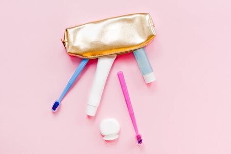 Teeth hygiene and oral dental care products in golden travel cosmetic purse kit pastel pink color background with copy space. Blank tube of toothpaste and toothbrushes. Flat lay, top view compositionの写真素材
