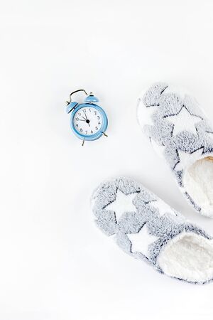 Sleep. Soft fluffy slippers and blue alarm clock isolated on white background. Creative conceptual top view flat lay in minimal style. Rest, good night, insomnia, relaxation, tired, hygge conceptの写真素材