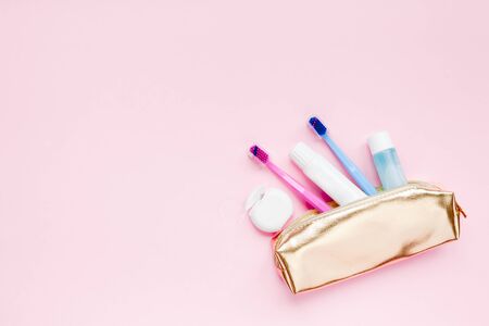 Teeth hygiene and oral dental care products in golden travel cosmetic purse kit pastel pink color background with copy space. Blank tube of toothpaste and toothbrushes. Flat lay, top view compositionの写真素材