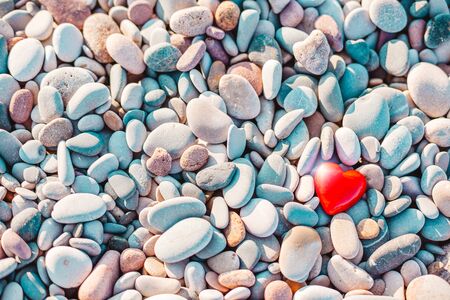 Valentines Day concept. Romantic love symbol of red heart on the pebble beach with copy space....