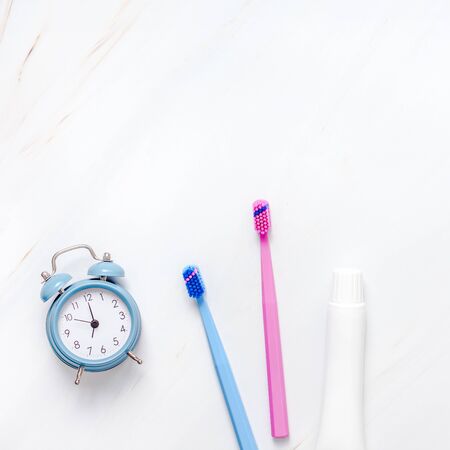 Teeth hygiene and oral dental care products with blue alarm clock on white marble table background with copy space. Blank tube of toothpaste and brushes. Flat lay, top view composition, mockupの写真素材