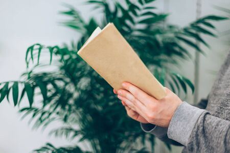 Young man reading open old paper book in the room with green plants, close up, vintage styleの写真素材