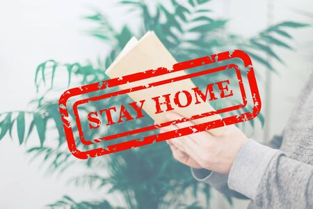 Stay home quarantine concept: Young man reading open old paper book in the room with green plants,...