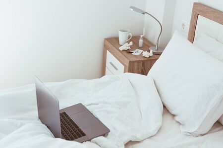 Working home quarantine self isolation lockdown concept. Laptop in unmade bed. Comfortable and cozy remote home office. Modern apartments with sunlight and minimalistic design. Stay safe in pandemic.の写真素材