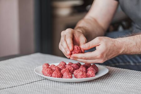 Man hands preparing meatballs with raw mincemeat. Lifestyle close up composition with natural light. Homemade cooking during lockdown, stay home housekeeping sharing concept. Side view with copy spaceの写真素材