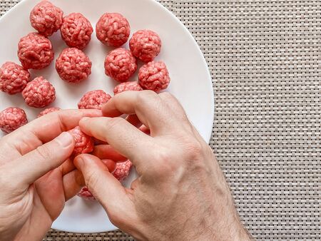 Man hands preparing meatballs with raw mincemeat. Lifestyle close up composition with natural light. Homemade cooking during lockdown, stay home housekeeping sharing concept. Top view with copy spaceの写真素材