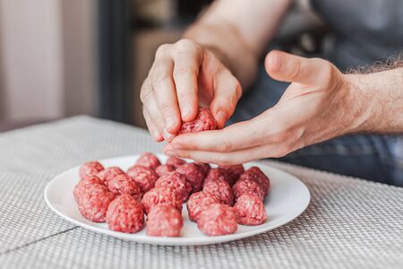 Man hands preparing meatballs with raw mincemeat. Lifestyle close up composition with natural light. Homemade cooking during lockdown, stay home housekeeping sharing concept. Side view with copy spaceの写真素材