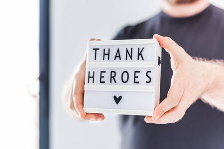 Nurse day concept. Man hands holding lightbox with Thank heroes text thanking doctors, nurses and medical staff working in hospitals during coronavirus COVID-19 pandemics. View through window glassの写真素材