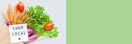 Fresh organic vegetables in eco craft paper shopping bag with text Shop Local on lightbox flat lay, top view with copy space on gray background. Sustainable lifestyle. Zero waste, plastic free concept.の写真素材