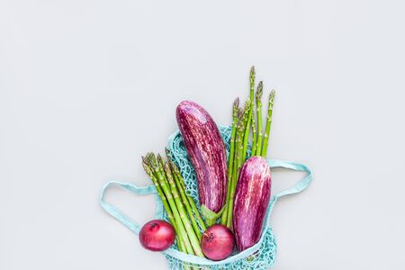Fresh organic vegetables in blue eco reusable cotton mesh shopping bag flat lay, top view with copy space on gray background. Sustainable lifestyle. Zero waste, plastic free concept.の写真素材