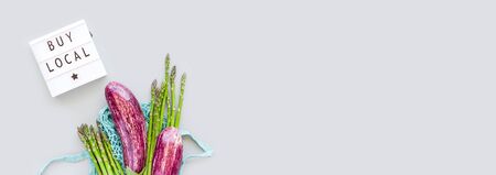 Fresh organic vegetables in eco cotton mesh shopping bag with text Buy Local on lightbox flat lay, top view with copy space on gray background. Sustainable lifestyle. Zero waste, plastic free concept.の写真素材