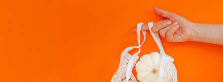Autumn flat lay composition with white pumpkins in mesh shopping bag on bold orange color background. Creative autumn, thanksgiving, fall, halloween concept in zero waste style. Top view, copy spaceの写真素材