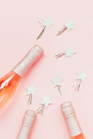 Christmas or New Year composition with bottles of rose champagne and golden shiny sparkle star confetti on pastel pink background, top view. Celebration flat lay. Party creative conceptの写真素材