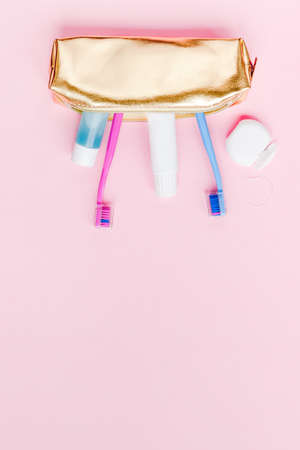 Teeth hygiene and oral dental care products in golden travel cosmetic purse kit on pastel pink color background with copy space. Blank tube of toothpaste and toothbrushes. Flat lay, top view compositionの写真素材