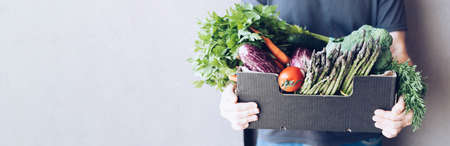 Fresh organic greens and vegetables delivery. Man hands holding box with farmer bio crop delivering in the house doorway. Small local business support. Online grocery shoppingの写真素材