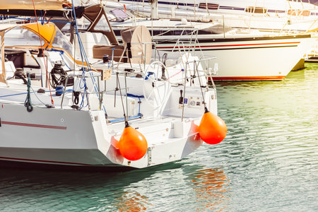 Yacht with orange buoys docked at marina, calm sea reflecting light,の写真素材