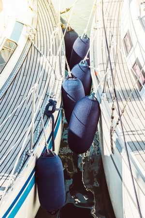 Sailboats with protective fenders anchored at marina, sunlight creating reflections,の写真素材