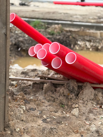 Red plastic construction pipes stacked at a muddy site, showing industrial building materials....