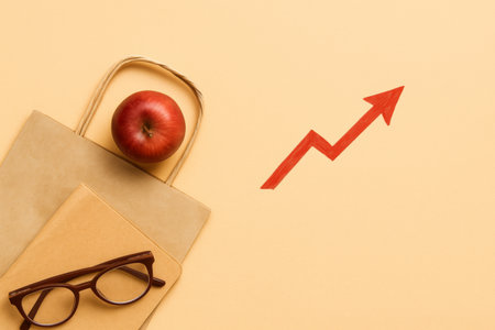 Flatlay concept with apple, glasses, notepad, and red arrow on beige background, AI generatedの素材