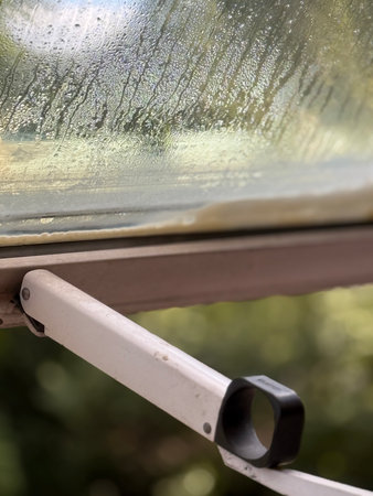 Rainy day seen through open window with raindrops on glass, creating natural background.
