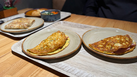 Omelets served on plates with assorted accompaniments on wooden table in restaurant setting. Mobile photoの写真素材