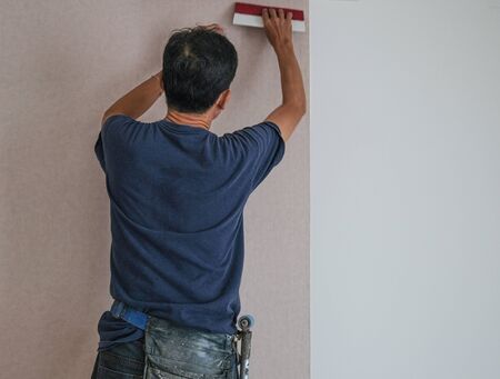 carpenter worker install wallpaper on white wallの写真素材