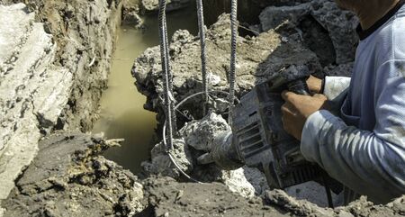 worker man use electric impact drill destroy concrete pole in big holeの写真素材