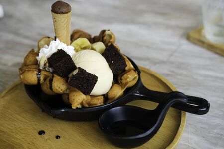 sweet dessert mix waffle ice cream banana cake. food contain in black bowl on wooden tray