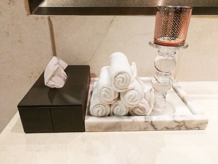 white roll hand towel prepare on marble tray. Tissue paper in wooden box. Candlestick grass put on counter restroomの写真素材