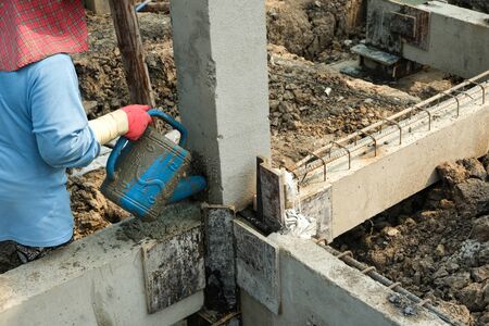 worker women use blue plastic watering can contain cement liquid into pillars hold dor building houseの写真素材