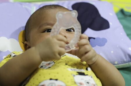 baby boy playing plastic toy for learning education while laying on bed.