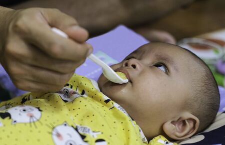 Father feeding mash banana fruit with plastic spoon to baby