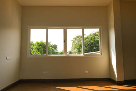 white wall in new house. wooden laminate floor in living room. big square windows clear glass green...