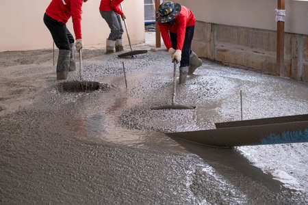 three worker team working wet cement  on floor by use trowel with long Tools spreading poured...