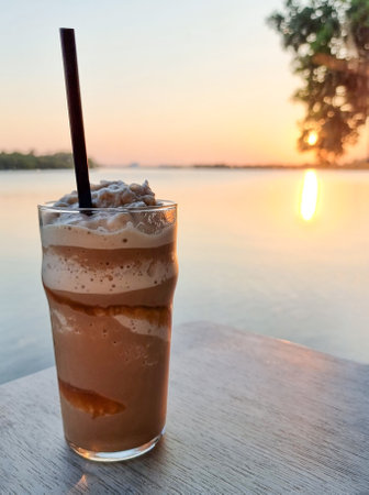 coffee smooties cool drinking water on the table wood sea and orange sunset down on water backgroundの写真素材