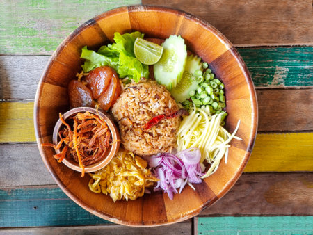 shrimp paste fried rice or kapi fried rice local thailand street food decoration with vegetable herb omelet onion cucumber in wooden plate.の写真素材
