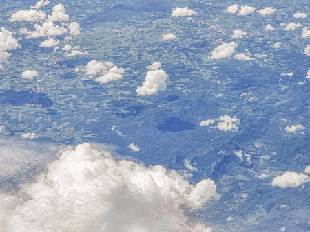 Abstract clouds floating in the sky above mountains and green trees captured from an aerial perspective.の写真素材