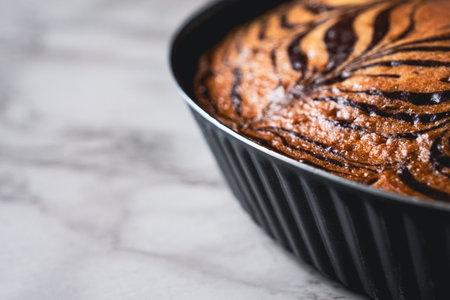 Zebra cake with a striped pattern baked in a metal dish, placed on a white marble tabletop, close-up view photo with copy space.の写真素材