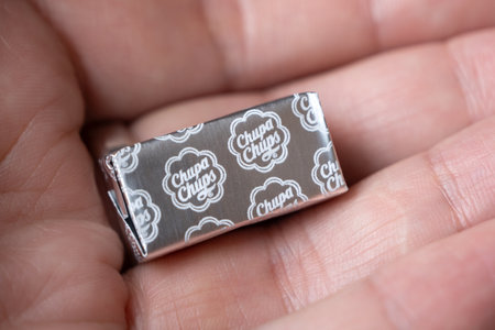 Close-up view of square shape Chupa Chups candy on the palm of the human hand, wrapped in silver...