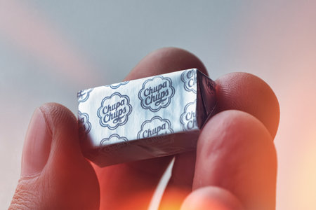 Close-up view of hand holding square shape Chupa Chups candy, wrapped in silver foil paper and...