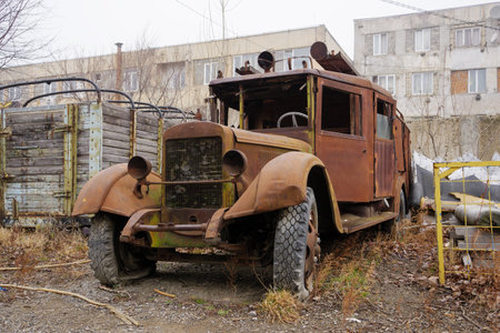 A rusty vintage Soviet truck stands abandoned by industrial buildings.