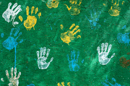 Various colorful handprints are painted on a textured green wall, creating an artistic urban street...