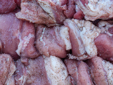 A close-up shot of raw meat cut into pieces, marinated with salt and pepper. The pieces are stacked and arranged in a closeup view, highlighting the texture and marination.の写真素材