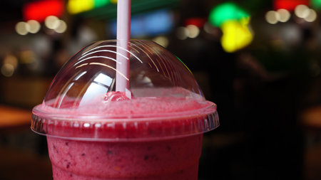 A close-up shot of a pink smoothie in a plastic cup with a straw, in a bright cafe setting. The smoothie is topped with a clear plastic dome lid.の写真素材